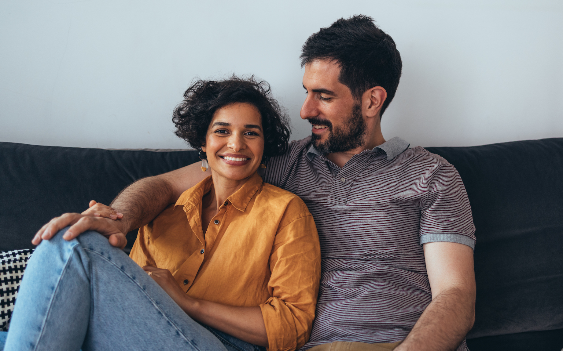 Couple relaxing on couch with woman smiling at camera and man looking at her