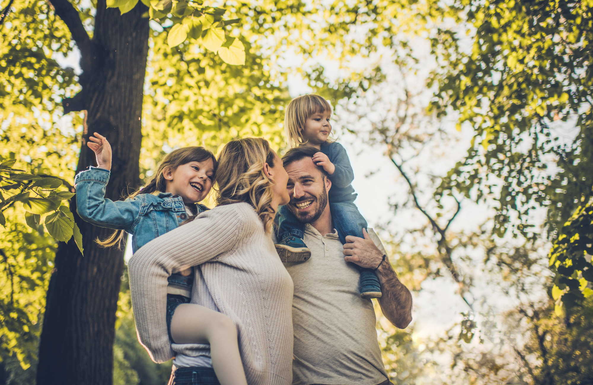 Parents carry two daughters on their shoulders in the park